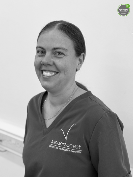A woman wearing a sandersonvet uniform is smiling at the camera, standing in front of a plain white background. A sticker that says Mental Health First Aider can be seen in the top right corner.