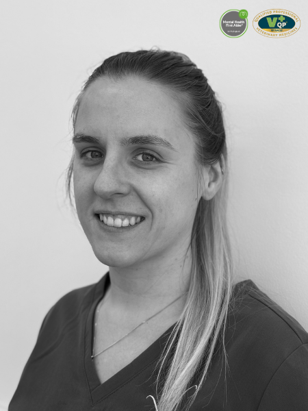 Black and white photo of a woman with long hair tied in a ponytail, wearing a scrub top and showing a small smile. There are two certificate logos in the upper right corner.