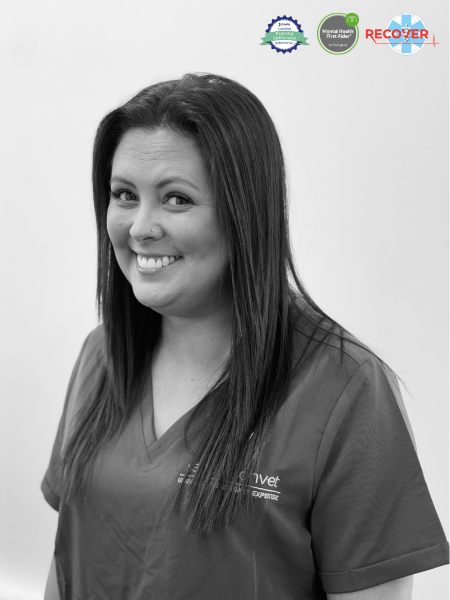 A woman with long straight hair is smiling at the camera while wearing medical scrubs. In the top right corner, there are three certification logos.