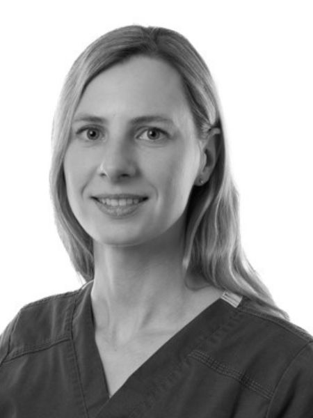 A woman with fair hair is wearing medical scrubs. She is facing the front and giving a slight smile. The background is plain white.