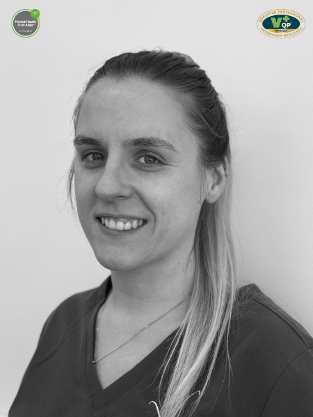 A black and white photo shows a woman with long hair in scrubs, smiling at the camera. There are two logos in the top corners of the picture.
