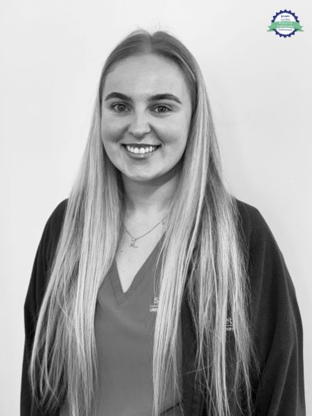 A woman with long, straight hair is smiling at the camera. She is wearing a V-neck top and a dark cardigan, and she is standing in front of a plain background.