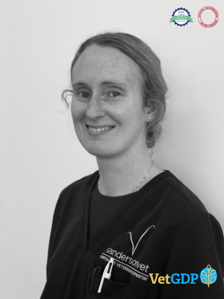 A woman wearing vet scrubs stands in front of a plain wall, smiling. At the bottom of the black and white picture, you can see some logos and the words VetGDP and Sanderson Vet.