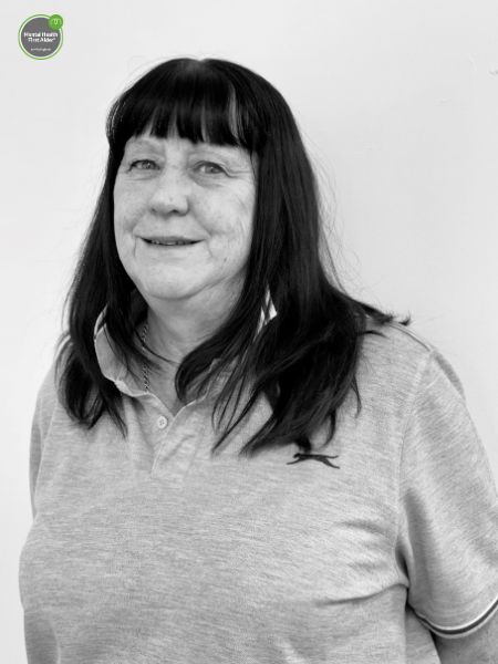 A woman with long dark hair and a fringe, dressed in a light polo shirt, stands in front of a plain light background.