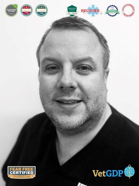 Black and white picture of a man in a dark shirt, smiling at the camera. Several veterinary certificate logos are shown in the top and bottom corners of the image.